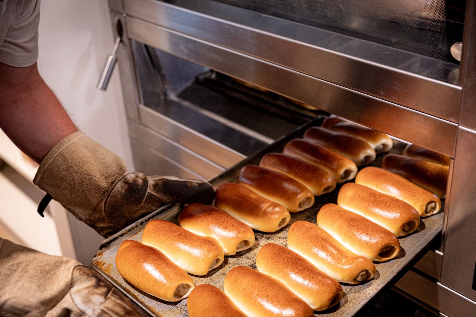 Bakker haalt een plaat vers afgebakken worstenbroodjes uit de winkeloven van Bakkerij van Hassel